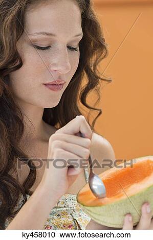 Stock Image - Close-up of a woman eating melon with a spoon. Fotosearch