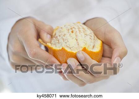 Stock Image - Close-up of a woman's hand peeling an orange. Fotosearch