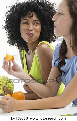 Stock Photograph - Close-up of two female friends eating fruits. Fotosearch