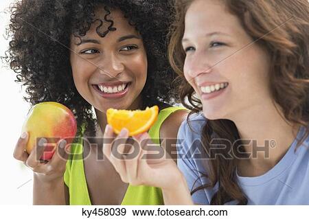 Close-up of two smiling female friends eating fruits View Large Photo Image Stock Photo - Close-up of two smiling female friends eating fruits. Fotosearch