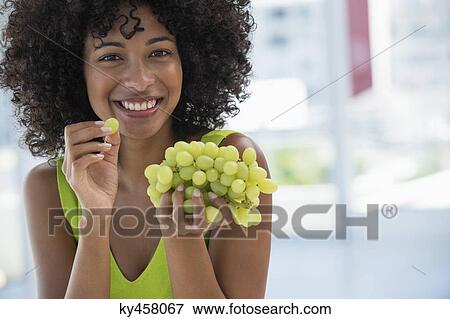 Stock Photo - Portrait of a smiling woman eating grapes. Fotosearch