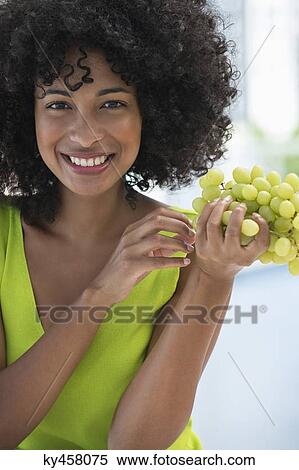 Stock Photography - Portrait of a smiling woman eating grapes. Fotosearch