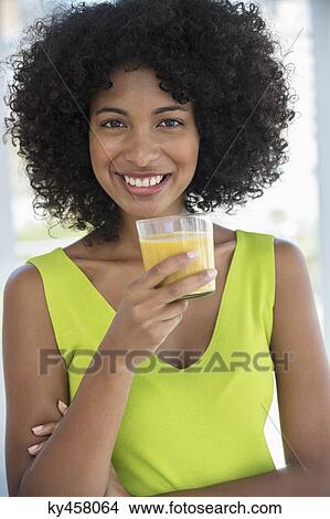 Portrait of a smiling woman holding a glass of mango shake View Large Photo Image Picture - Portrait of a smiling woman holding a glass of mango shake. Fotosearch