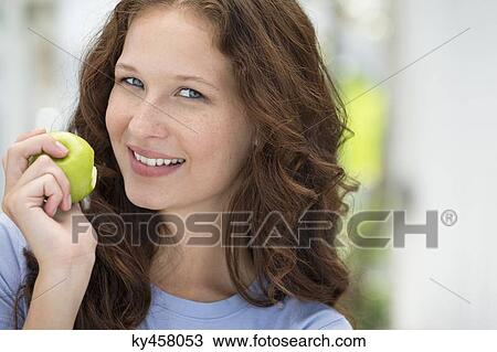 Stock Image - Portrait of a woman eating a green apple. Fotosearch
