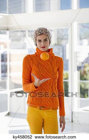 Stock Image - Portrait of a woman tossing an orange. Fotosearch