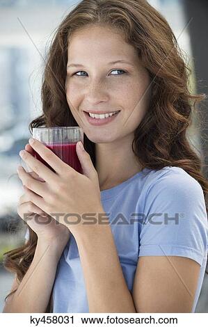 Stock Image - Smiling woman holding a glass of pomegranate juice. Fotosearch