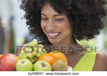 Stock Image - Smiling woman holding a plate of fruits. Fotosearch