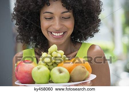 Smiling woman holding a plate of fruits View Large Photo Image Stock Image - Smiling woman holding a plate of fruits. Fotosearch