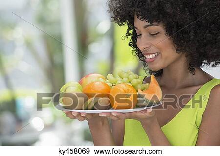Smiling woman holding a plate of fruits View Large Photo Image Stock Photo - Smiling woman holding a plate of fruits. Fotosearch