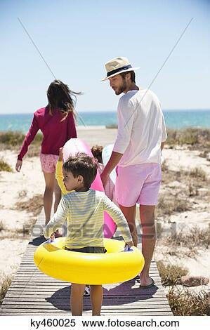 Stock Photography - Children with their parents holding inflatable rings on a boardwalk on the beach. Fotosearch