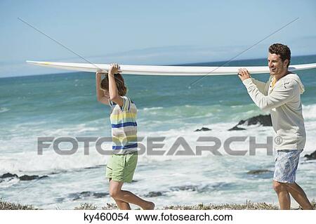 Man and his son carrying a surfboard on the beach View Large Photo Image Picture - Man and his son carrying a surfboard on the beach. Fotosearch