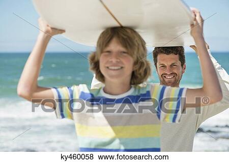 Man and his son carrying a surfboard on the beach View Large Photo Image Stock Photo - Man and his son carrying a surfboard on the beach. Fotosearch