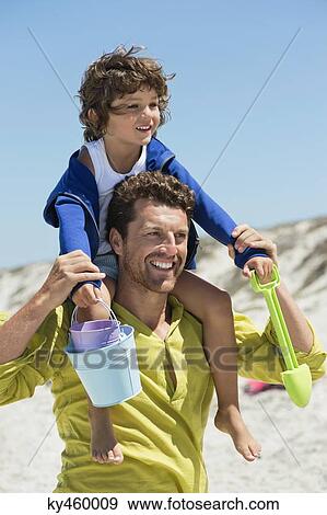 Stock Photo - Man carrying his son on shoulders on the beach. Fotosearch