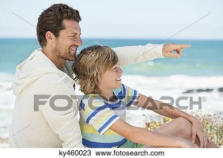 Stock Image - Man pointing with his son on the beach. Fotosearch