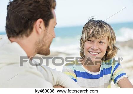 Man sitting with his son on the beach View Large Photo Image Stock Photograph - Man sitting with his son on the beach. Fotosearch