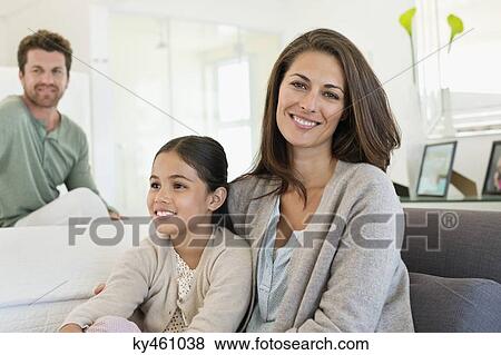 Smiling woman sitting with her daughter and her husband in the background View Large Photo Image Stock Photo - Smiling woman sitting with her daughter and her husband in the background. Fotosearch
