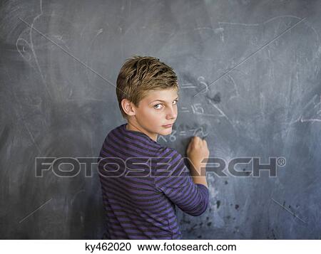 Stock Image - Boy writing on a blackboard in a classroom. Fotosearch
