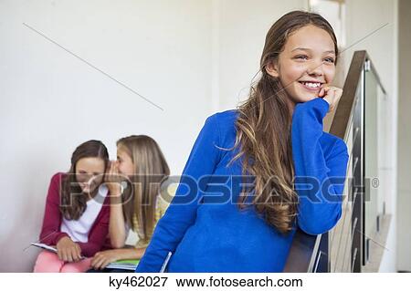 Stock Photo - Close-up of a girl smiling with her friends whispering in the background. Fotosearch