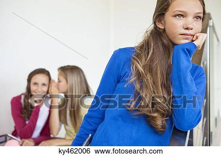 Stock Photograph - Close-up of a girl thinking with her friends whispering in the background. Fotosearch