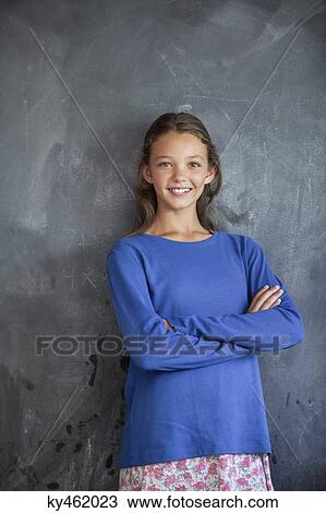Stock Image - Girl smiling with his arms crossed in front of a blackboard in a classroom. Fotosearch