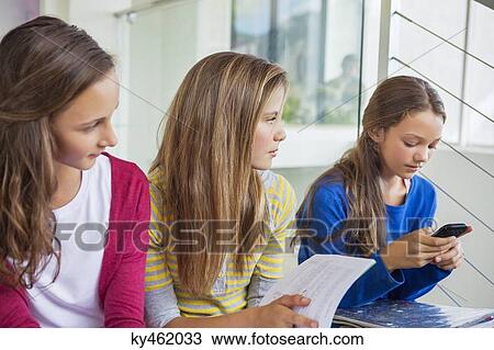Girl using a mobile phone and her friends looking at her View Large Photo Image Stock Image - Girl using a mobile phone and her friends looking at her. Fotosearch