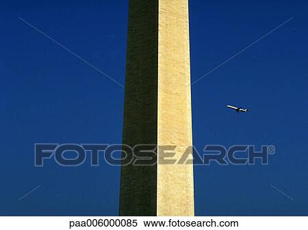 Stock Photography - Plane flying in sky behind concrete structure. Fotosearch