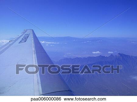 Stock Photograph - Plane wing during flight over mountains. Fotosearch