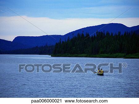 Stock Image - Rowboat on water, mountains in background.. Fotosearch