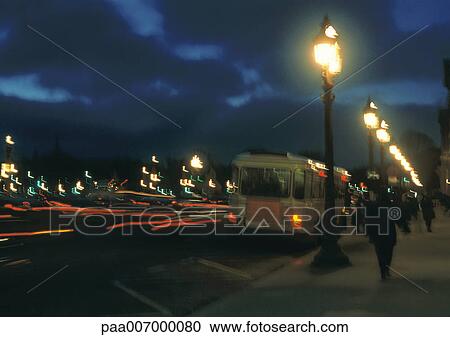 Stock Image - France, Paris, bus stopped next to sidewalk at night. Fotosearch