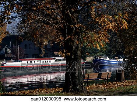 Stock Photo - Barges docked in river, tree in foreground. Fotosearch