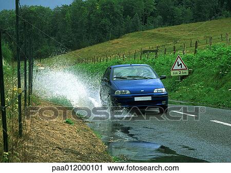 Stock Image - Car driving through puddle, splashing water. Fotosearch
