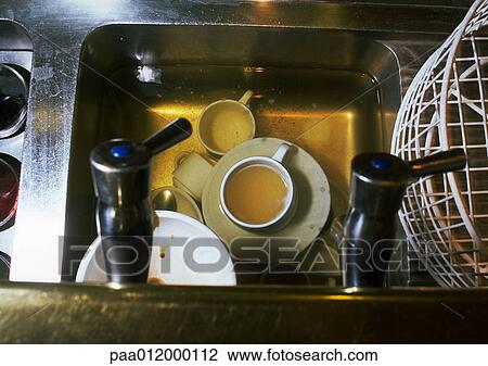 Stock Image - Dirty dishes soaking in water in sink, high angle view. Fotosearch