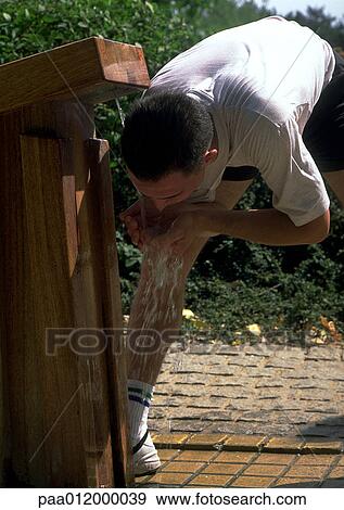 Man bending over cupping water from spout into mouth View Large Photo Image Stock Photo - Man bending over cupping water from spout into mouth . Fotosearch