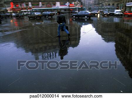 Picture - Person walking through square on wet ground with reflection. Fotosearch