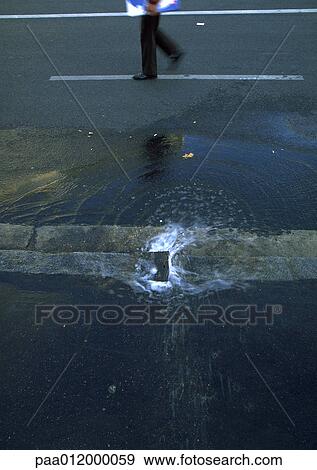 Stock Photo - Pool of water on street and person walking, low section. Fotosearch