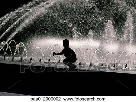 Stock Image - Silhouette of boy crouching on edge of fountain. Fotosearch