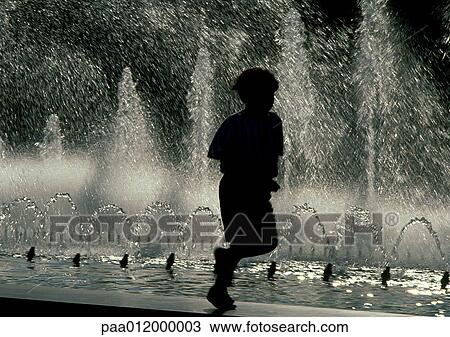 Stock Image - Silhouette of boy crouching on edge of fountain. Fotosearch