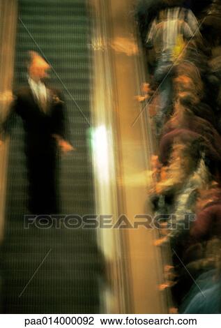 Crowd of people going up an escalator, one man coming down, blurred. View Large Photo Image Stock Image - Crowd of people going up an escalator, one man coming down, blurred.. Fotosearch