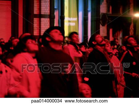 Picture - Crowd of people looking up with a pink hue shinning down, blurred.. Fotosearch