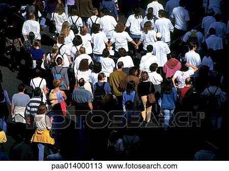 Stock Image - Crowd of people, many in white shirts, high angle view. Fotosearch