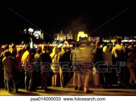 Stock Image - Crowd of people standing at night, blurred. Fotosearch