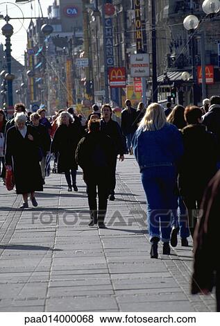 Stock Photo - Crowd walking down sidewalk on a cold day, buildings in background.. Fotosearch