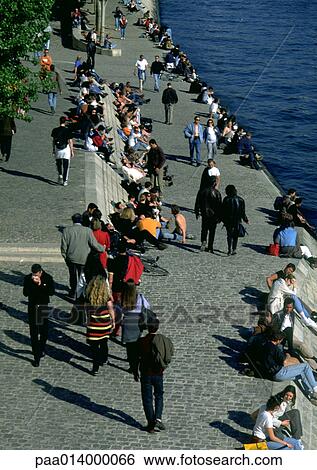 Stock Photograph - People walking and sitting by water. Fotosearch