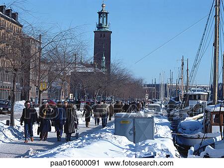 Stock Image - Sweden, Stockholm, people walking alongside quay with docked boats. Fotosearch