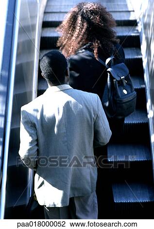 Stock Image - Couple riding escalator, rear view.. Fotosearch