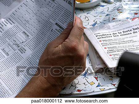 Stock Image - Man reading newspaper at table, close up of paper.. Fotosearch