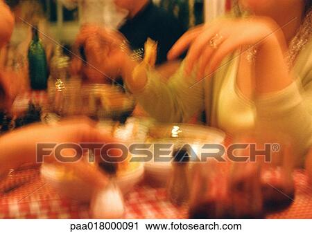 Stock Image - People eating at table in restaurant, blurred.. Fotosearch
