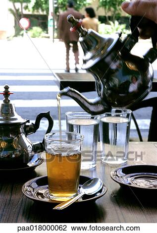 Person pouring tea into glass, people crossing street in background View Large Photo Image Stock Image - Person pouring tea into glass, people crossing street in background. Fotosearch