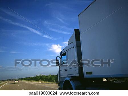 Picture - Semi-truck on highway, partial view, road and blue sky in background. Fotosearch