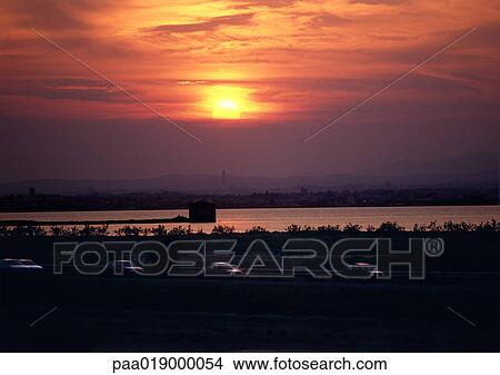 Picture - Sunset over water and traffic on freeway. Fotosearch